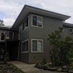 Two-storey modern house with dark grey weatherboard exterior and garden landscaping.