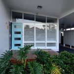Front entrance with blue door, large windows with white shutters, and greenery.