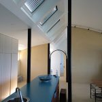 Modern kitchen with skylights, blue countertop island, and black support poles.