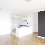 Open-plan kitchen and living area with timber flooring and dark feature wall.