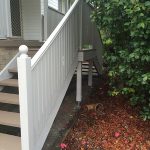 Outdoor staircase with grey railing beside garden bed.