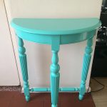 Half-moon turquoise wooden table with decorative legs.