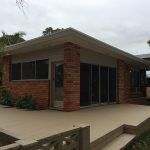 Brick house with large windows, flat roof, and concrete patio.