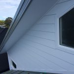 House exterior with white cladding, gable roof, and window.