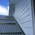 Close-up of house exterior with white cladding and corrugated metal roof.