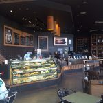 Coffee shop interior with pastry display counter, menu boards, and seating area.