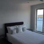 Bedroom with neatly made bed, white bedding, and large window overlooking water.