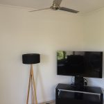 Living room corner with flat-screen TV on stand, floor lamp, and ceiling fan.