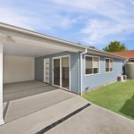 Backyard view of blue house with covered patio and lawn.